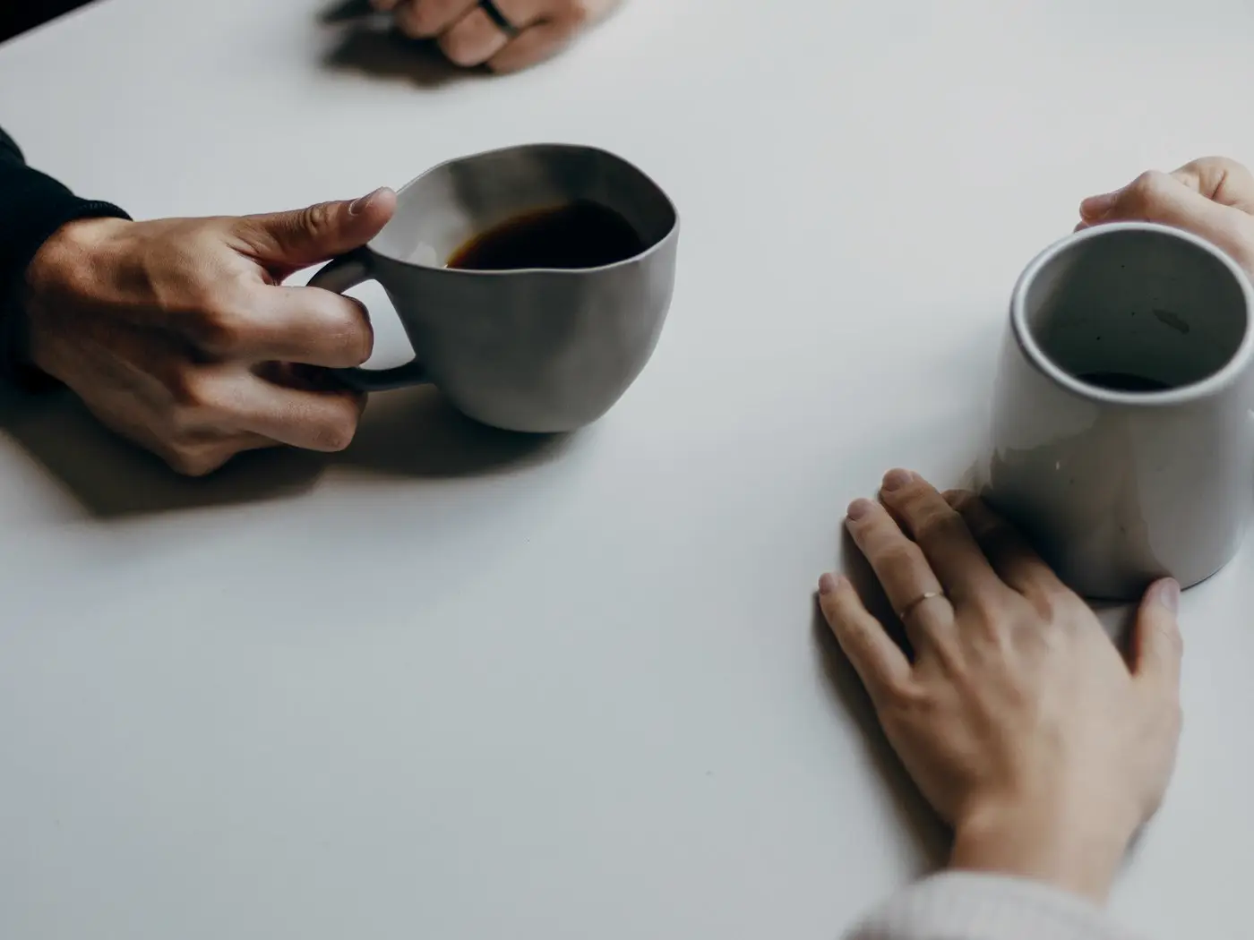 Deux personnes face à face à une table blanche, chacune tenant une tasse de café