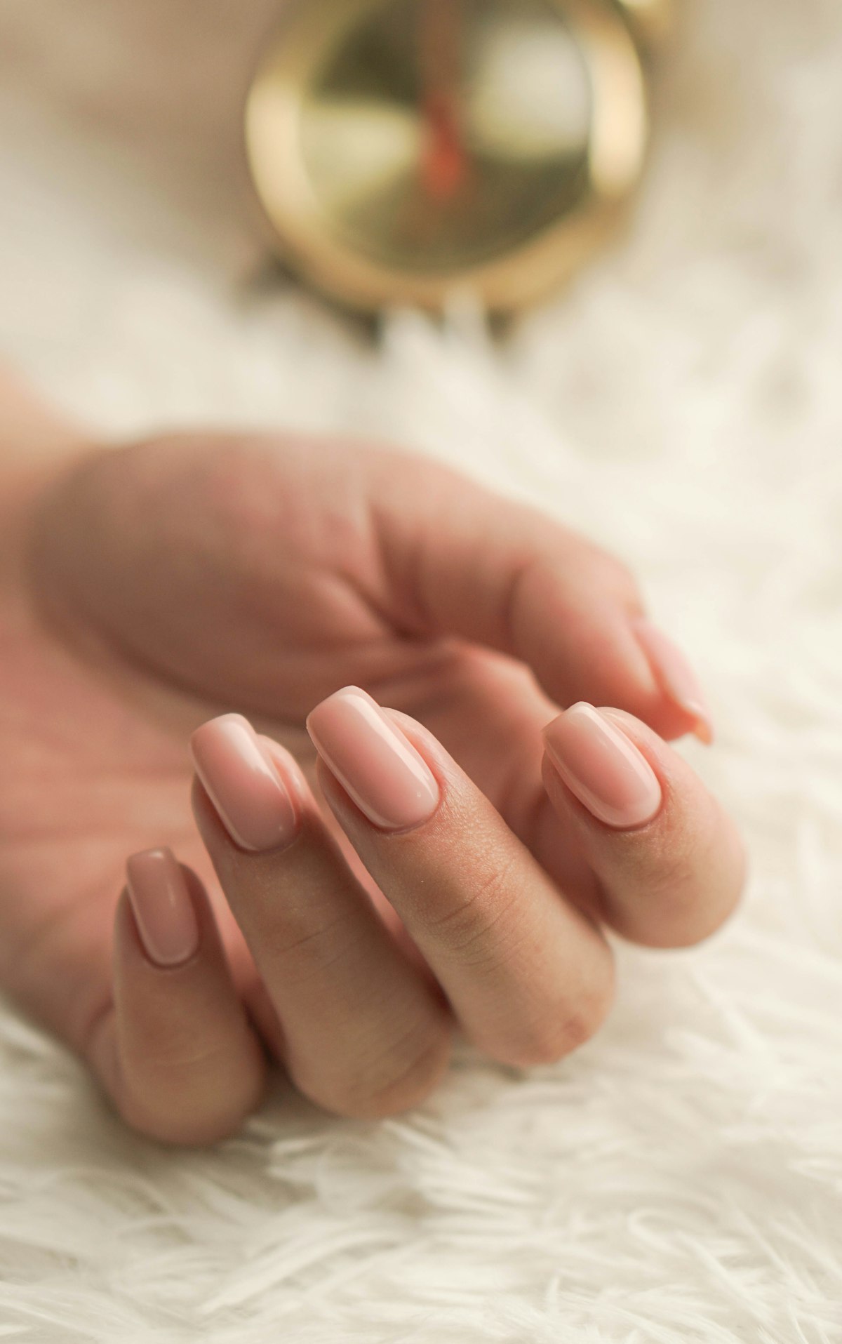Main aux ongles rose pâle sur un tissu blanc