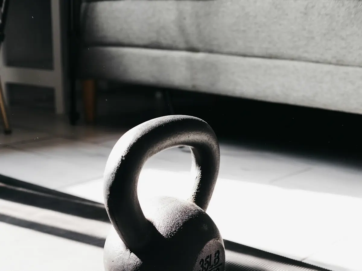 Un kettlebell posé sur le carrelage d'un salon, devant un canapé, dans la lumière du matin