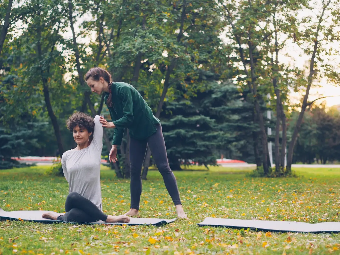 Une coach corrige la posture d'une femme assise sur un tapis, dans un parc en automne